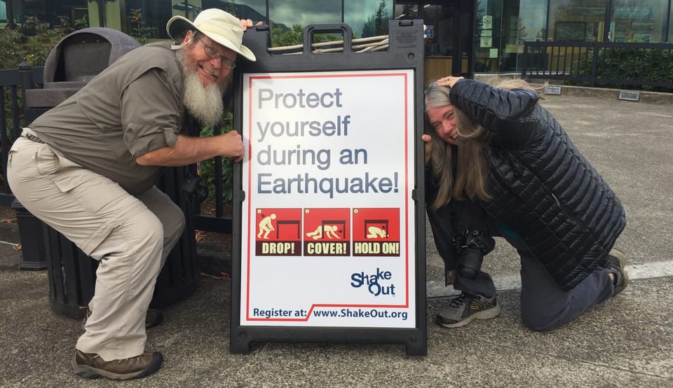 Man and woman cowering with a Protect Yourself during an Earthquake sign between them
